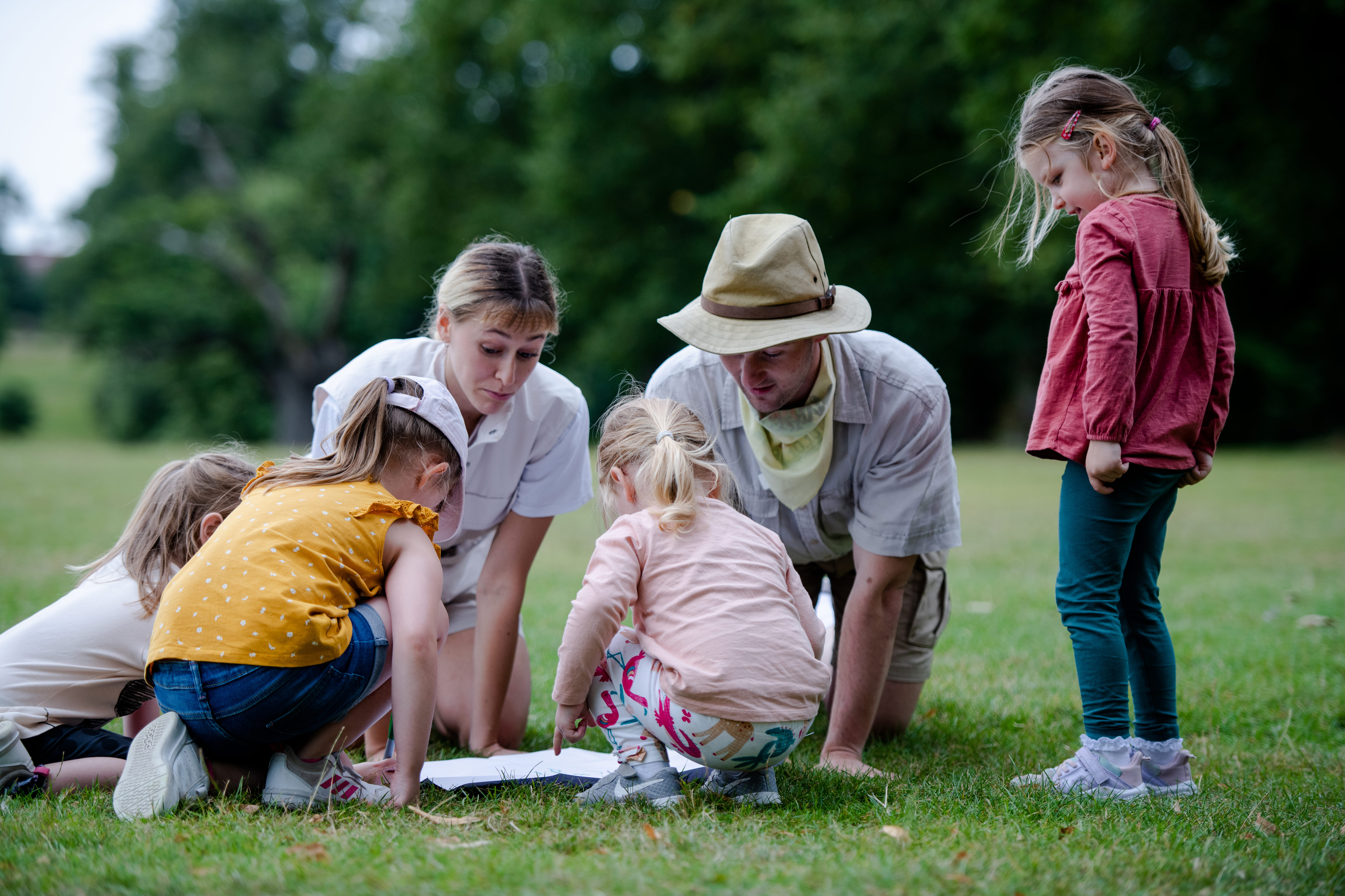 children and adults grouped around a book on the grass